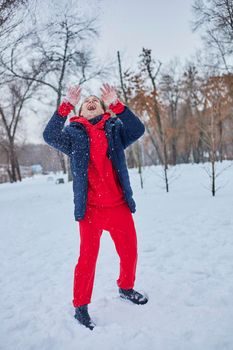 a young happy man is having fun in a winter park, throwing snow, it is cold in his hands, the emissions are off scale