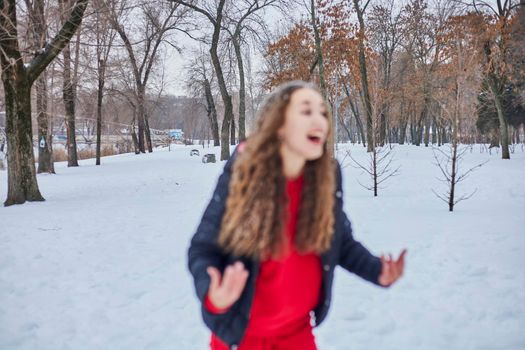 a young happy woman is having fun in a winter park, throwing snow, it is cold in her hands, the emissions are off scale