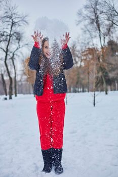 a young happy woman is having fun in a winter park, throwing snow, it is cold in her hands, the emissions are off scale