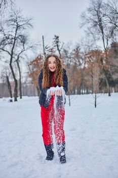 a young happy woman is having fun in a winter park, throwing snow, it is cold in her hands, the emissions are off scale