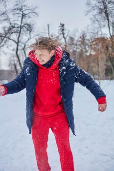 a young happy man is having fun in a winter park, throwing snow, it is cold in his hands, the emissions are off scale