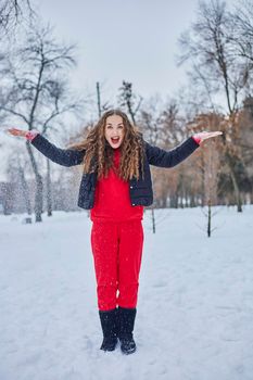 a young happy woman is having fun in a winter park, throwing snow, it is cold in her hands, the emissions are off scale