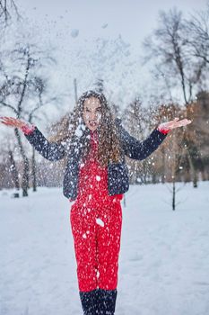 a young happy woman is having fun in a winter park, throwing snow, it is cold in her hands, the emissions are off scale