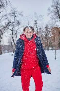 a young happy man is having fun in a winter park, throwing snow, it is cold in his hands, the emissions are off scale