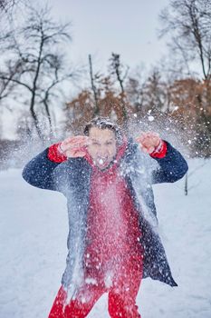 a young happy man is having fun in a winter park, throwing snow, it is cold in his hands, the emissions are off scale