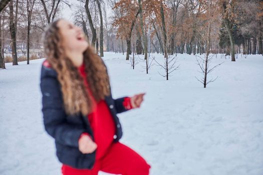 a young happy woman is having fun in a winter park, throwing snow, it is cold in her hands, the emissions are off scale