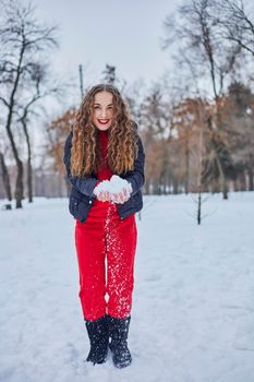 a young happy woman is having fun in a winter park, throwing snow, it is cold in her hands, the emissions are off scale