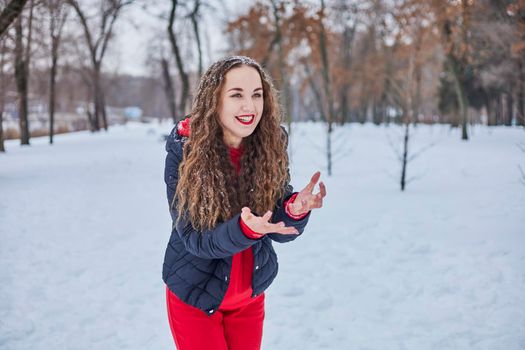 a young happy woman is having fun in a winter park, throwing snow, it is cold in her hands, the emissions are off scale