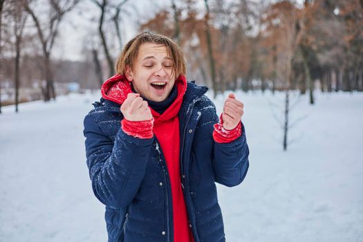 a young happy man is having fun in a winter park, throwing snow, it is cold in his hands, the emissions are off scale