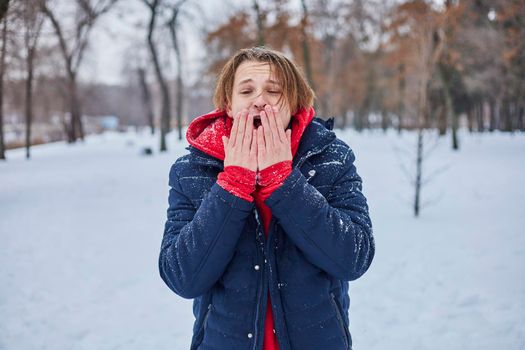 a young happy man is having fun in a winter park, throwing snow, it is cold in his hands, the emissions are off scale