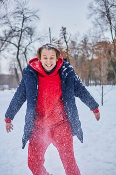 a young happy man is having fun in a winter park, throwing snow, it is cold in his hands, the emissions are off scale