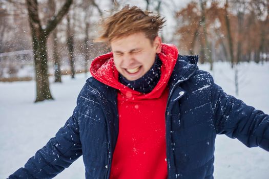 a young happy man is having fun in a winter park, throwing snow, it is cold in his hands, the emissions are off scale