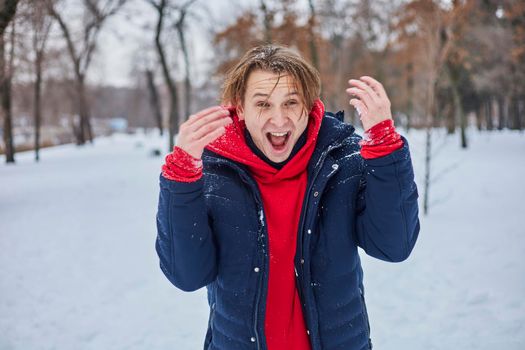 a young happy man is having fun in a winter park, throwing snow, it is cold in his hands, the emissions are off scale