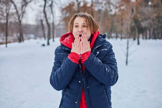 a young happy man is having fun in a winter park, throwing snow, it is cold in his hands, the emissions are off scale