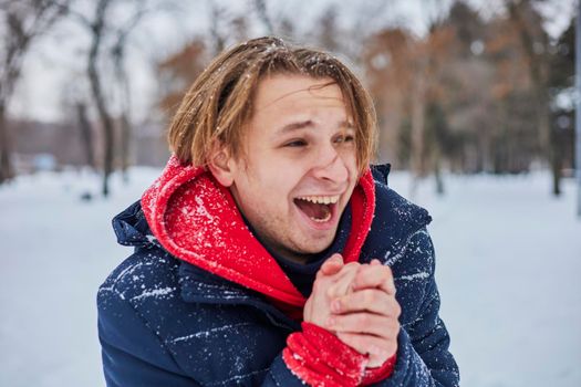 a young happy man is having fun in a winter park, throwing snow, it is cold in his hands, the emissions are off scale