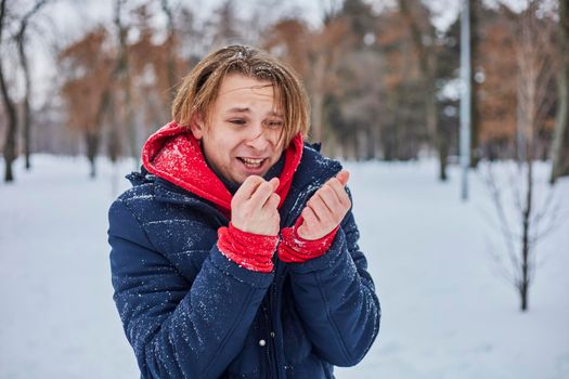 a young happy man is having fun in a winter park, throwing snow, it is cold in his hands, the emissions are off scale