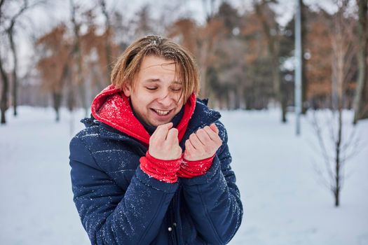 a young happy man is having fun in a winter park, throwing snow, it is cold in his hands, the emissions are off scale