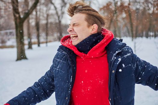 a young happy man is having fun in a winter park, throwing snow, it is cold in his hands, the emissions are off scale