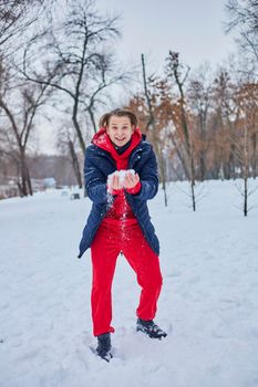 a young happy man is having fun in a winter park, throwing snow, it is cold in his hands, the emissions are off scale