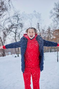 a young happy man is having fun in a winter park, throwing snow, it is cold in his hands, the emissions are off scale