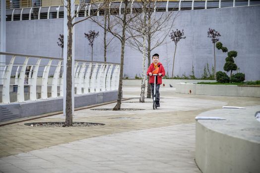 Happy family lifestyle and holiday concept. One little boy riding scooter, walking in city, street. Having fun alone.