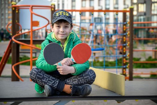 Happy ping pong player think about a game. young boy sitting after match on a tennis table outdoors.