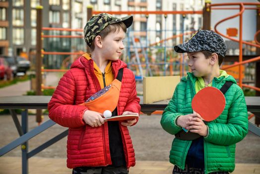 Two happy boys, teenager twin brothers, enjoying vacation playing ping pong outdoors. Active leisure for children concept.