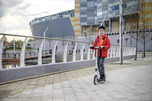 Happy family lifestyle and holiday concept. One little boy riding scooter, walking in city, street. Having fun alone.