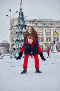 young family guy and girl spend the day in the park on a snowy day. Emotional young couple having fun while walking in the winter city, a lively man hugs his laughing beautiful woman