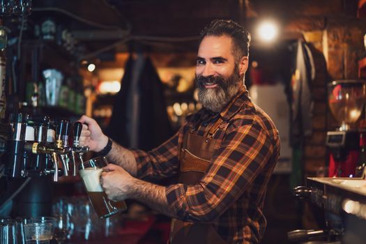 Portrait of cheerful barmen at pub. He pours beer into a beer glass.