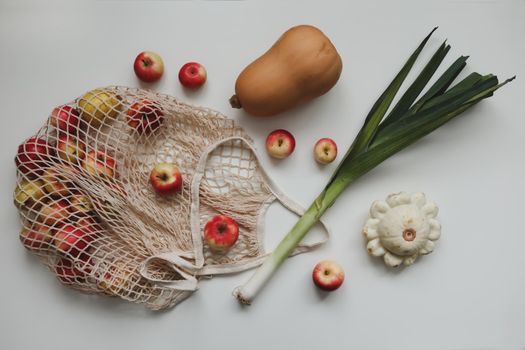autumn harvest with sqush, pumpkin, apples and vegetables in mesh shopping bag on white background