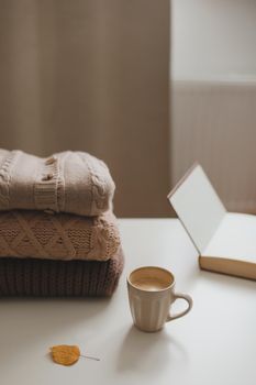 cozy home atmosphere and still life with a cup, candle and sweaters on a table.