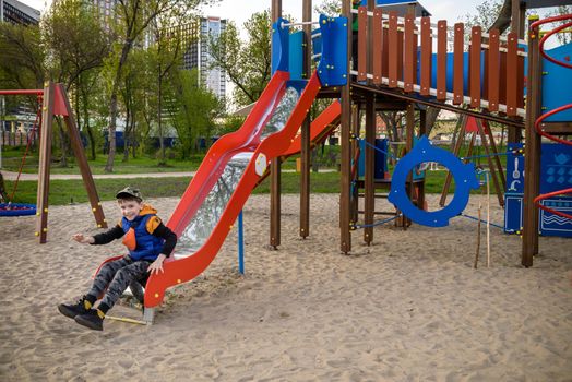 Portrait of cute boy playing on slide at playground on sunny morning.