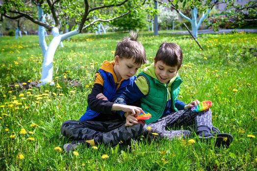 children playing with colorful toys Pop It. Boys on vacation. Tired of games, relaxing on the grass. Summer time for children, two boys friends at reboot together.