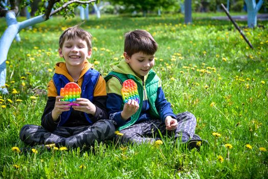 children playing with colorful toys Pop It. Boys on vacation. Tired of games, relaxing on the grass. Summer time for children, two boys friends at reboot together.