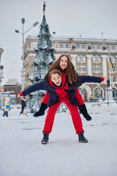 young family guy and girl spend the day in the park on a snowy day. Emotional young couple having fun while walking in the winter city, a lively man hugs his laughing beautiful woman