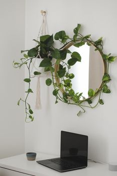 cozy workplace with a laptop on the table and a flower by the round mirror. home interior decoration