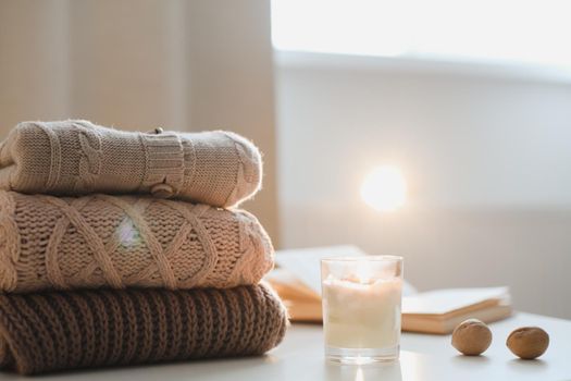 cozy home atmosphere and still life with a cup, candle, book and sweaters on a table.
