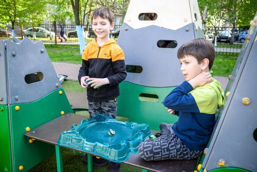 Two Boys playing with modern spin top outdoors. Entertainment game for children. Top, triggered by a trigger. Kids having a tournament on arena or battle field.