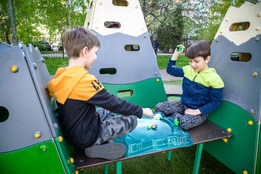 Two Boys playing with modern spin top outdoors. Entertainment game for children. Top, triggered by a trigger. Kids having a tournament on arena or battle field.