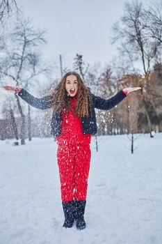 a young happy woman is having fun in a winter park, throwing snow, it is cold in her hands, the emissions are off scale