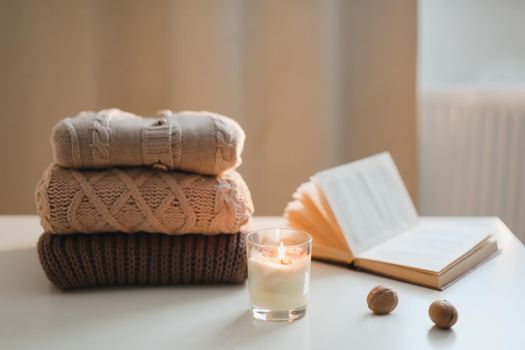 cozy home atmosphere and still life with a cup, candle and sweaters on a table.