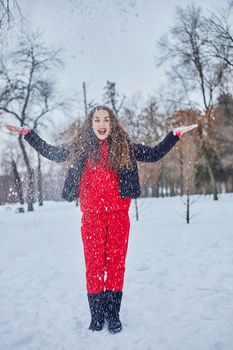 a young happy woman is having fun in a winter park, throwing snow, it is cold in her hands, the emissions are off scale