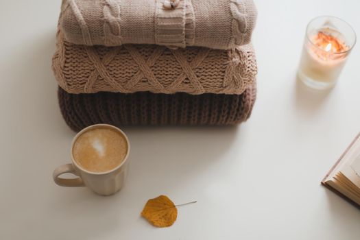 cozy home atmosphere and still life with a cup, candle and sweaters on a table.