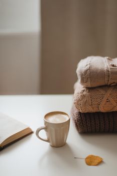 cozy home atmosphere and still life with a cup, candle and sweaters on a table.