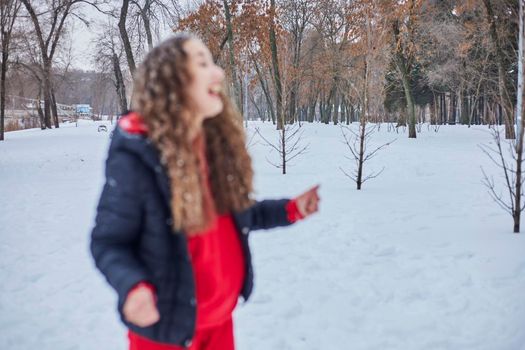 a young happy woman is having fun in a winter park, throwing snow, it is cold in her hands, the emissions are off scale