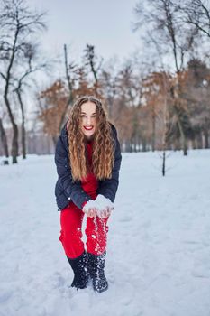 a young happy woman is having fun in a winter park, throwing snow, it is cold in her hands, the emissions are off scale