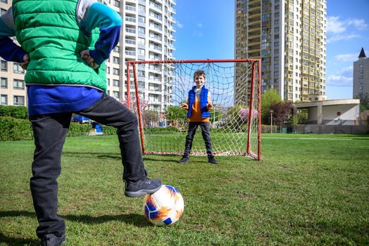 Little preschool boys friends playing soccer football on playground grass field outside. Happy authentic candid childhood lifestyle. Seasonal summer outdoor activity with ball for kids.