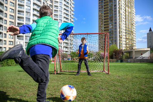 Little preschool boys friends playing soccer football on playground grass field outside. Happy authentic candid childhood lifestyle. Seasonal summer outdoor activity with ball for kids.