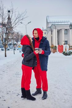 young family guy and girl spend the day in the park on a snowy day. the guy hugs the girl while standing on the street, they drink coffee together